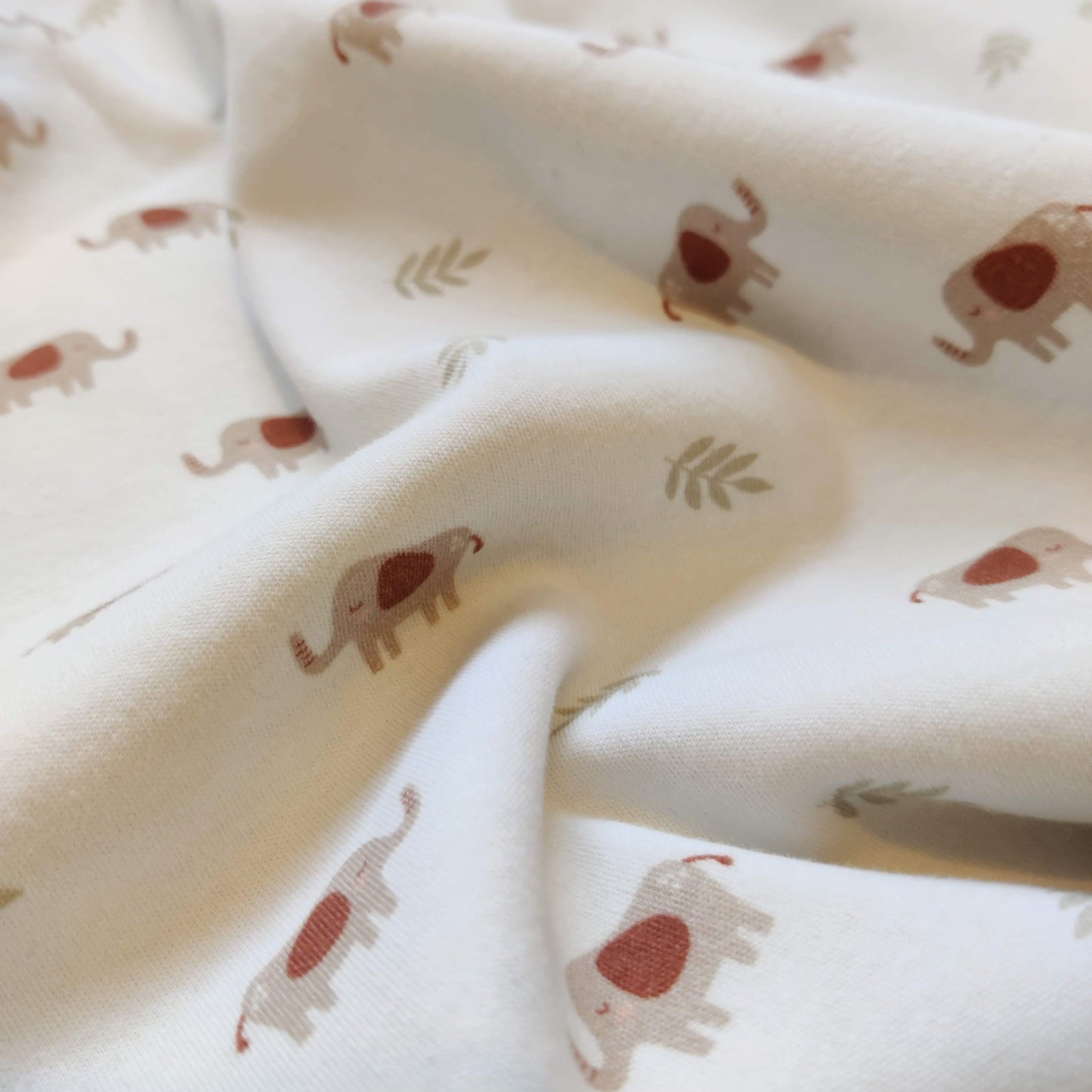 Close up of a cotton blanket with elephants and leaves on a white background