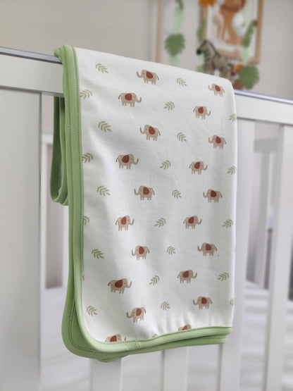 Safari themed blanket folded and draped over a cot, with an animal crib mobile in the background