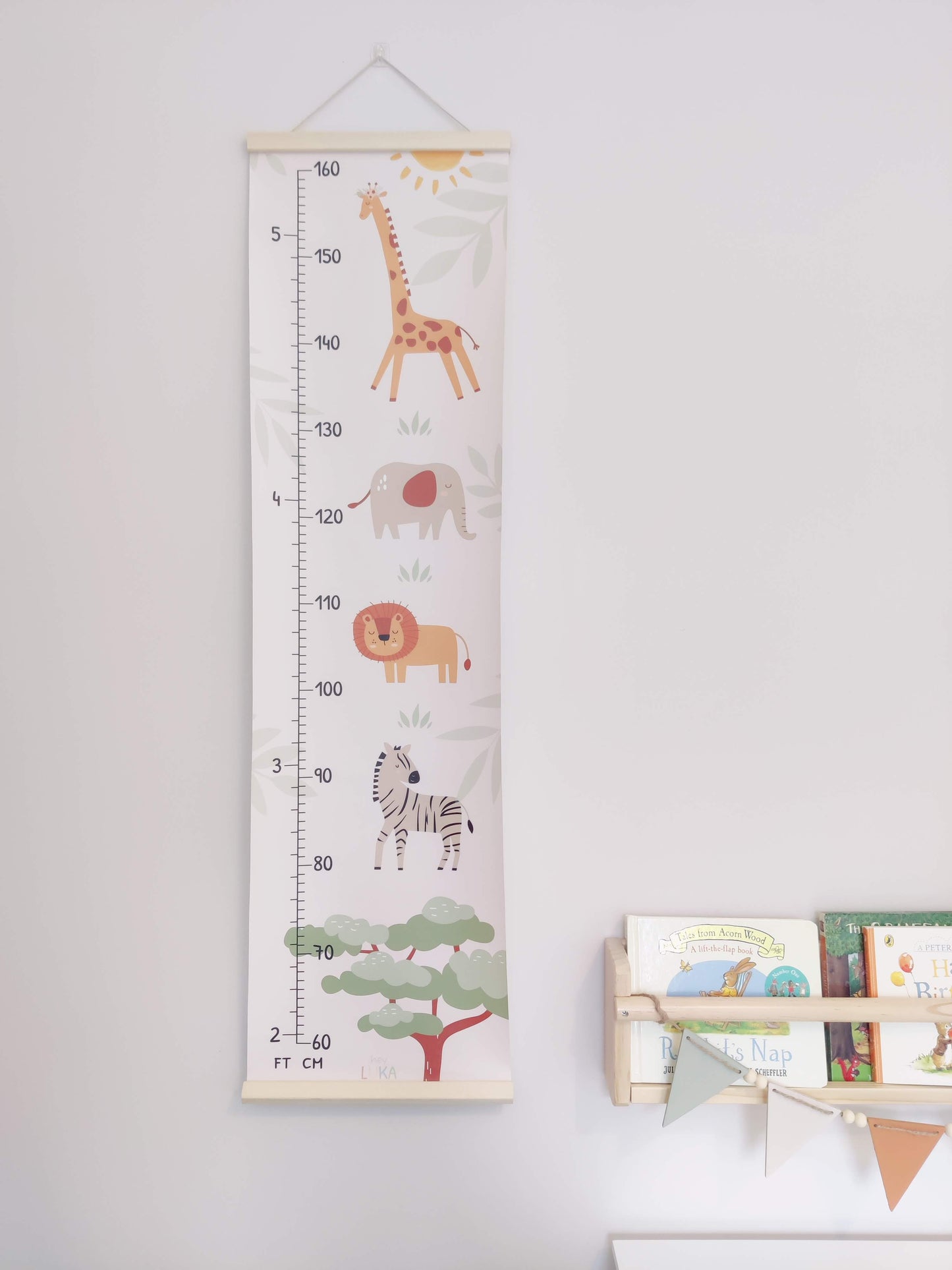 Neutral coloured height chart with safari animals hanging on a wall next to a kids bookshelf