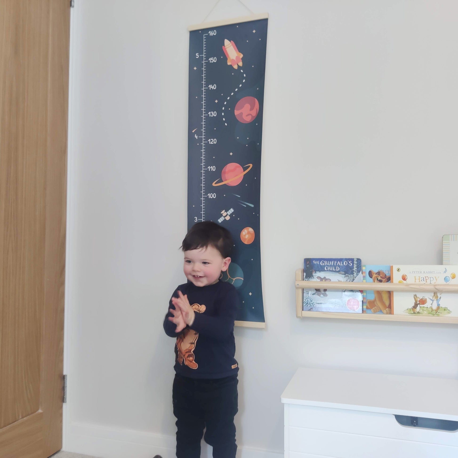 Heightchart with planets and rocket illustration in a space theme with young boy stood in front clapping his hands