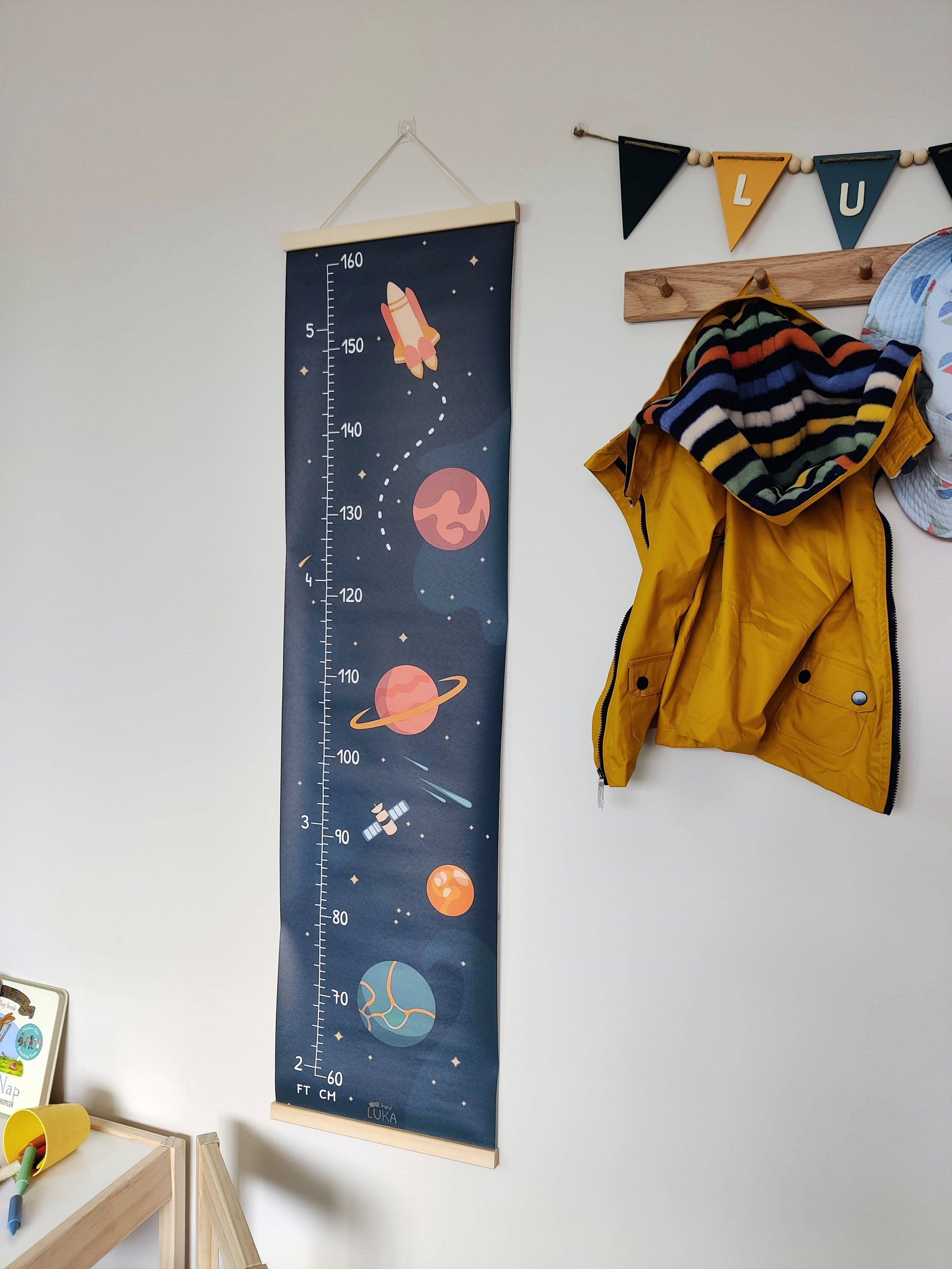 Space-themed height chart in a kid’s bedroom with hanging décor.