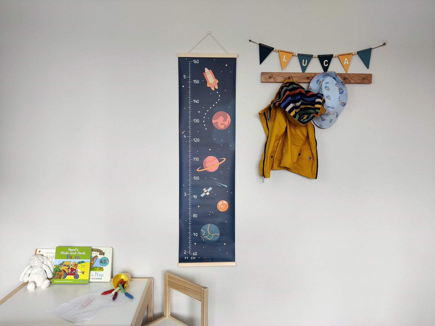 Space height chart with imperial and metric measurements, in a bold colour scheme. It is hanging on a neutral wall with matching wooden bunting flags spelling 'Luca'