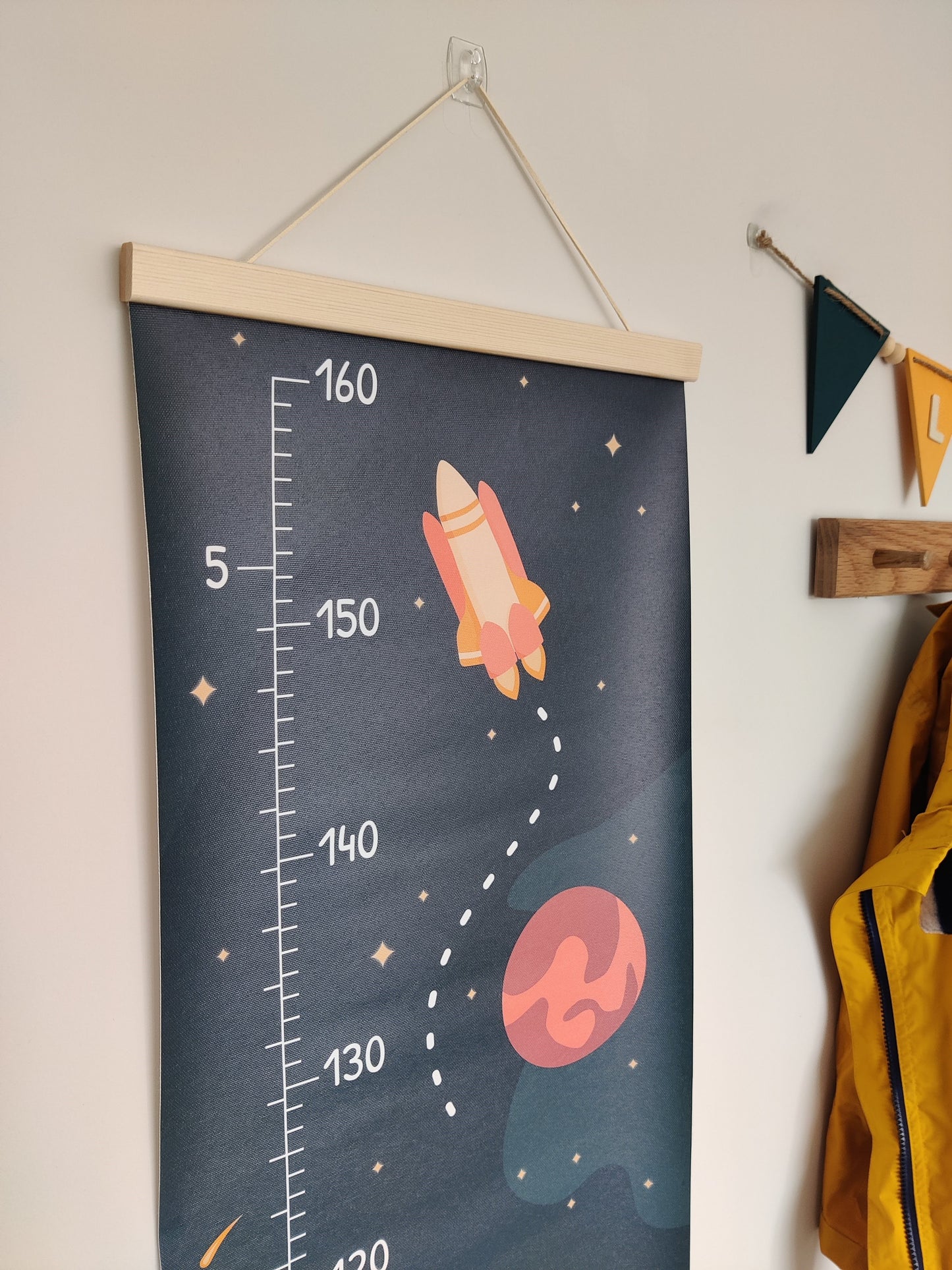 Close up of a canvas height chart with a planet, rocket and stars on the top. The canvas is framed with a wooden hanger.
